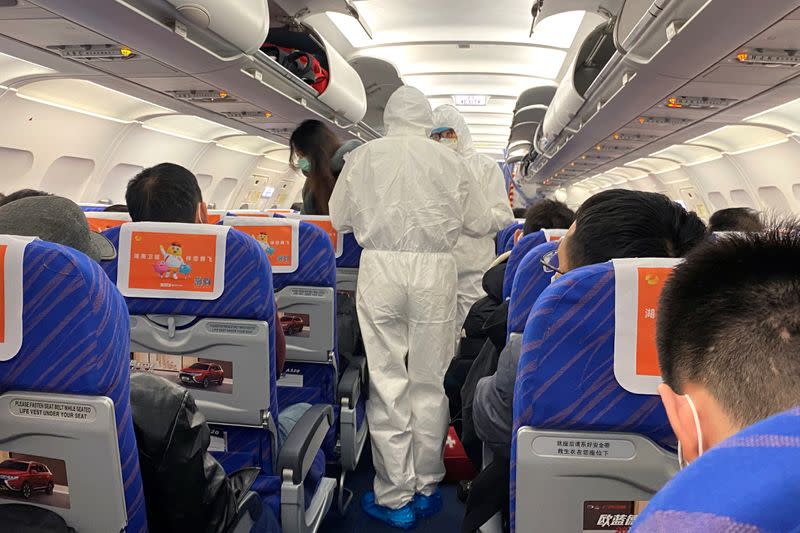 Trabajadores de salud con trajes protectores verifican la condición de un pasajero en un avión que acaba de aterrizar desde Changsha, una ciudad en una provincia vecina al centro del brote de coronavirus, en Shanghái, China.