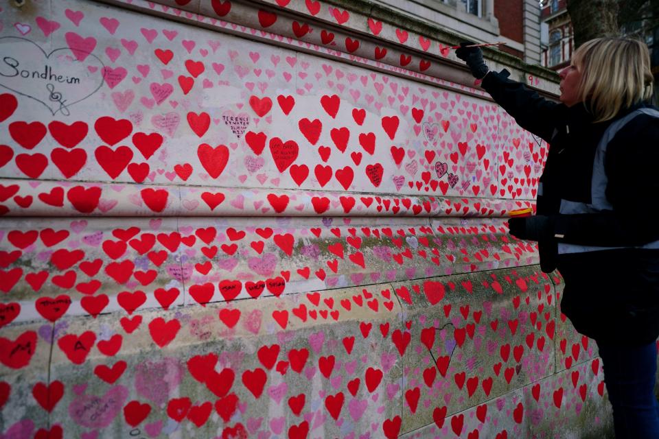 A volunteer from the Covid-19 Bereaved Families for Justice campaign group paints a heart on a memorial wall in London (PA Wire)