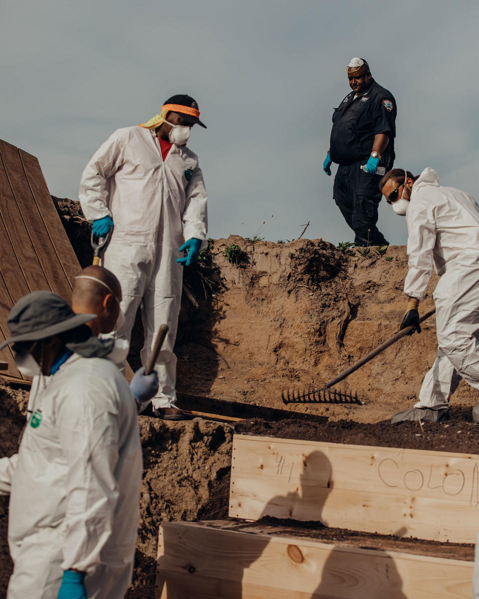 Workers place pine caskets inside a mass grave on Hart Island while correction officers look on.<span class="copyright">Sasha Arutyunova for TIME</span>