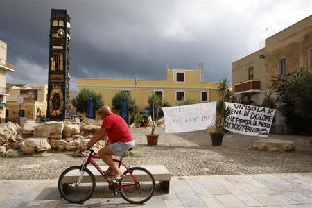 A man cycles past banners, which read: "An island full of pain that bears the indifference of the world" (R) and "Lampedusa wants to welcome immigrants alive, not dead", in the centre of the southern Italian island of Lampedusa October 4, 2013. REUTERS/Antonio Parrinello