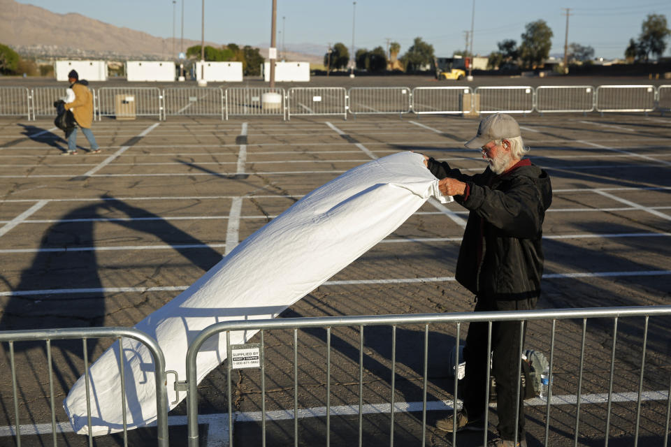 A man prepares a place to sleep on the ground of a parking lot at a makeshift camp for the homeless Monday, March 30, 2020, in Las Vegas. Officials opened part of the lot as a makeshift homeless shelter after a local shelter closed when a man staying there tested positive for the coronavirus. (AP Photo/John Locher)