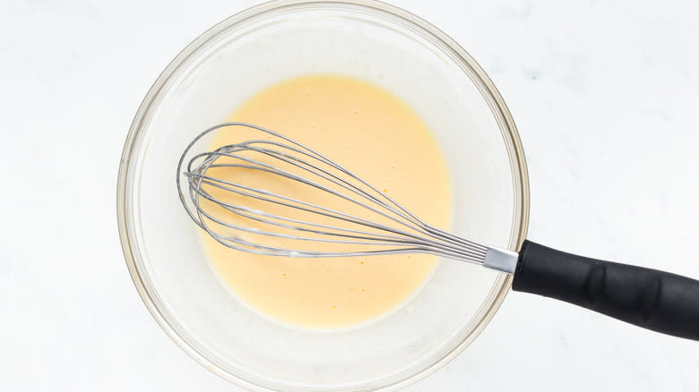 Egg and milk mixture in bowl with whisk