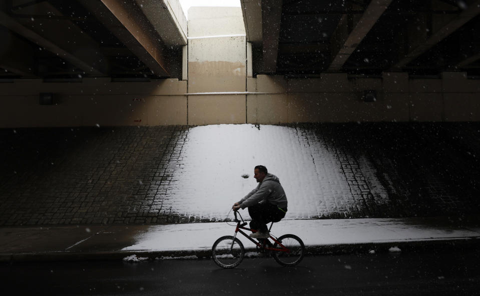 A cyclist rides under an overpass as snow falls, Friday, January 19, 2024, in Philadelphia. (Yong Kim/The Philadelphia Inquirer via AP)