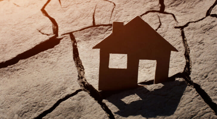 Flat cut-out image of house jammed into the crack of dry desert, symbolizing housing crisis