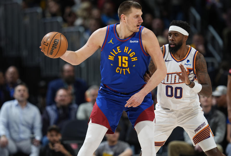 Denver Nuggets center Nikola Jokic, left, looks to pass the ball as Phoenix Suns forward Royce O'Neale defends during the first half of an NBA basketball game Tuesday, March 5, 2024, in Denver. (AP Photo/David Zalubowski)