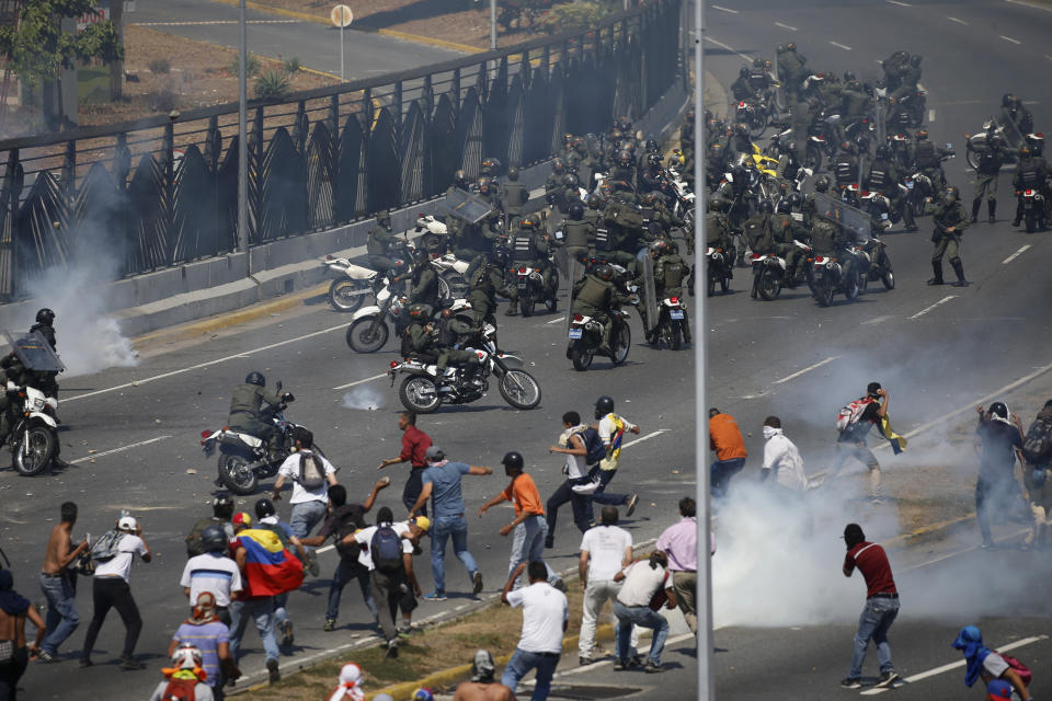 Opositores al presidente venezolano Nicolás Maduro, abajo, se enfrentan con tropas leales de la Guardia Nacional Bolivariana, que les disparan gas lacrimógeno, frente a la base aérea militar de La Carlota, en Caracas, el martes 30 de abril de 2019. (Foto AP/Fernando Llano)