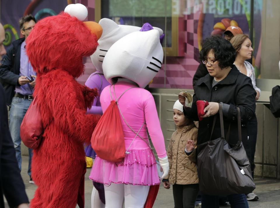 A woman gives a monetary tip to characters in New York's Times Square after she photographed the girl with them, Tuesday, April 9, 2013.  A string of arrests in the last few months has brought unwelcome attention to the growing number of people, mostly poor immigrants, who make a living by donning character outfits, roaming Times Square and charging tourists a few dollars to pose with them in photos. (AP Photo/Richard Drew)