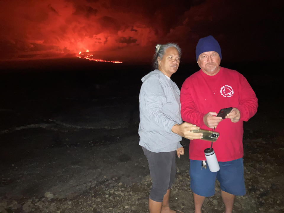 Willette Kalaokahaku Akima-Akau, left, and her husband Eddie Akau stand at a spot overlooking lava flowing from Mauna Loa on Tuesday, Nov. 29, 2022 in Hilo, Hawaii. For Akima-Akau and other Native Hawaiians, the eruption brings deep and personal cultural significance. (AP Photo/Caleb Jones)