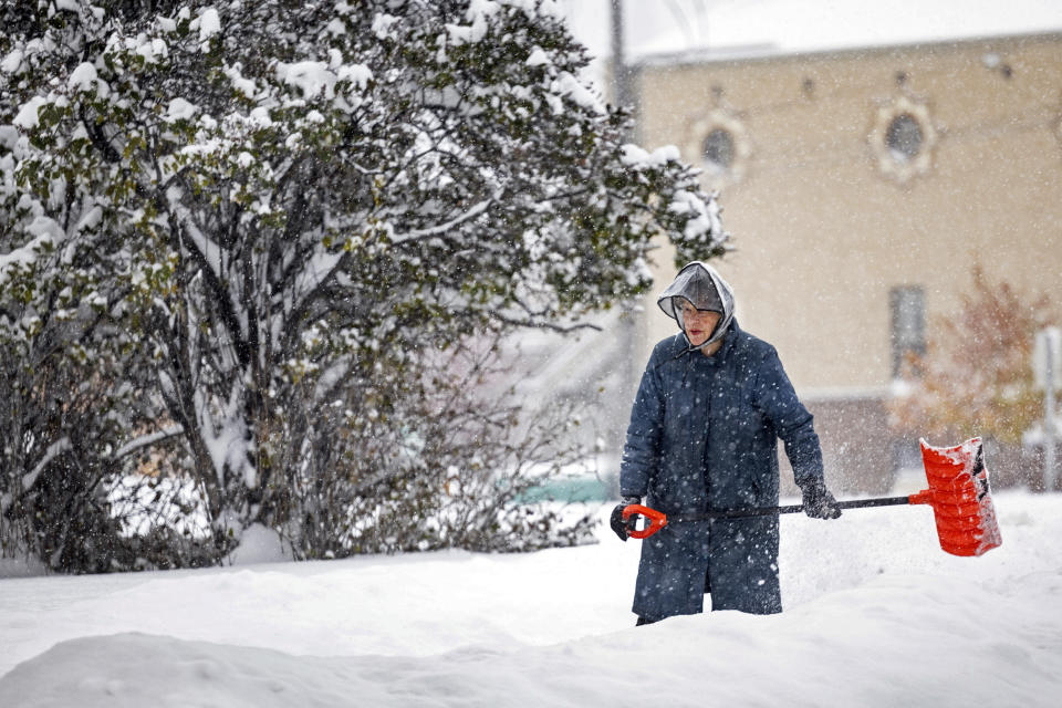 A woman shovel snow, Wednesday, Oct. 25, 2023, in Helena, Mont. The first major snowstorm of the season dropped up to a foot of snow in the Helena area by Wednesday morning, canceling some school bus routes. (Thom Bridge/Independent Record via AP)