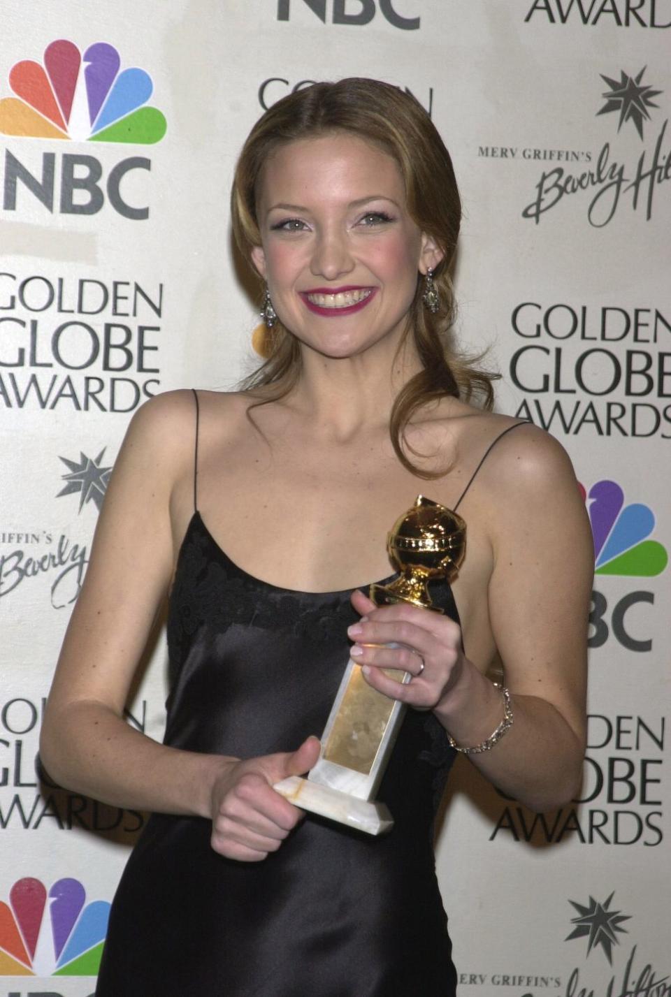 kate hudson in a black dress and smiling as she holds her golden globe trophy