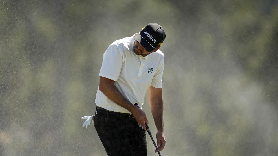 Jason Day shields himself from windswept sand at the 18th hole. - Ashley Landis/AP