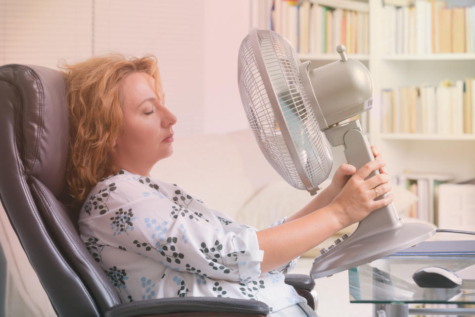 Woman suffers from heat while working in the office and tries to cool off by the fan