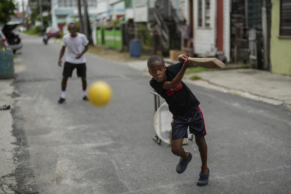 Dos personas juegan al críquet en una calle en el vecindario de Charlestown, en Georgetown, Guyana, el 2 de junio de 2024. Guyana es una de las sedes de la Copa Mundial de Críquet T20. (AP Foto/Ramón Espinosa)