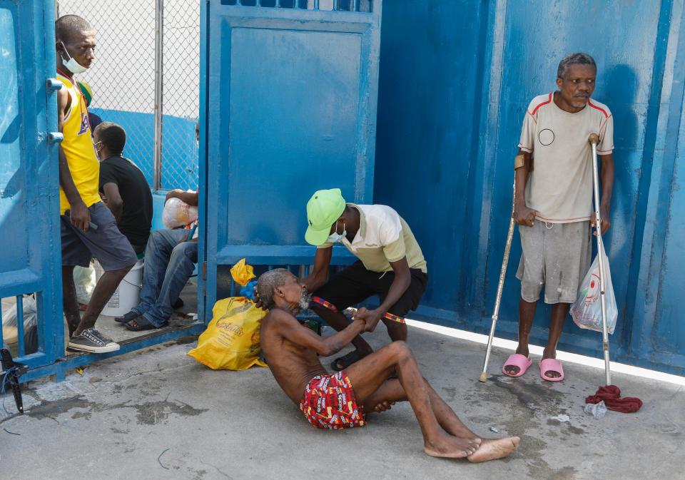 An inmate comes to the aide of a prisoner after armed gangs freed thousands from the National Penitentiary, in Port-au-Prince, Haiti, Saturday, March 3, 2024. (AP Photo/Odelyn Joseph)