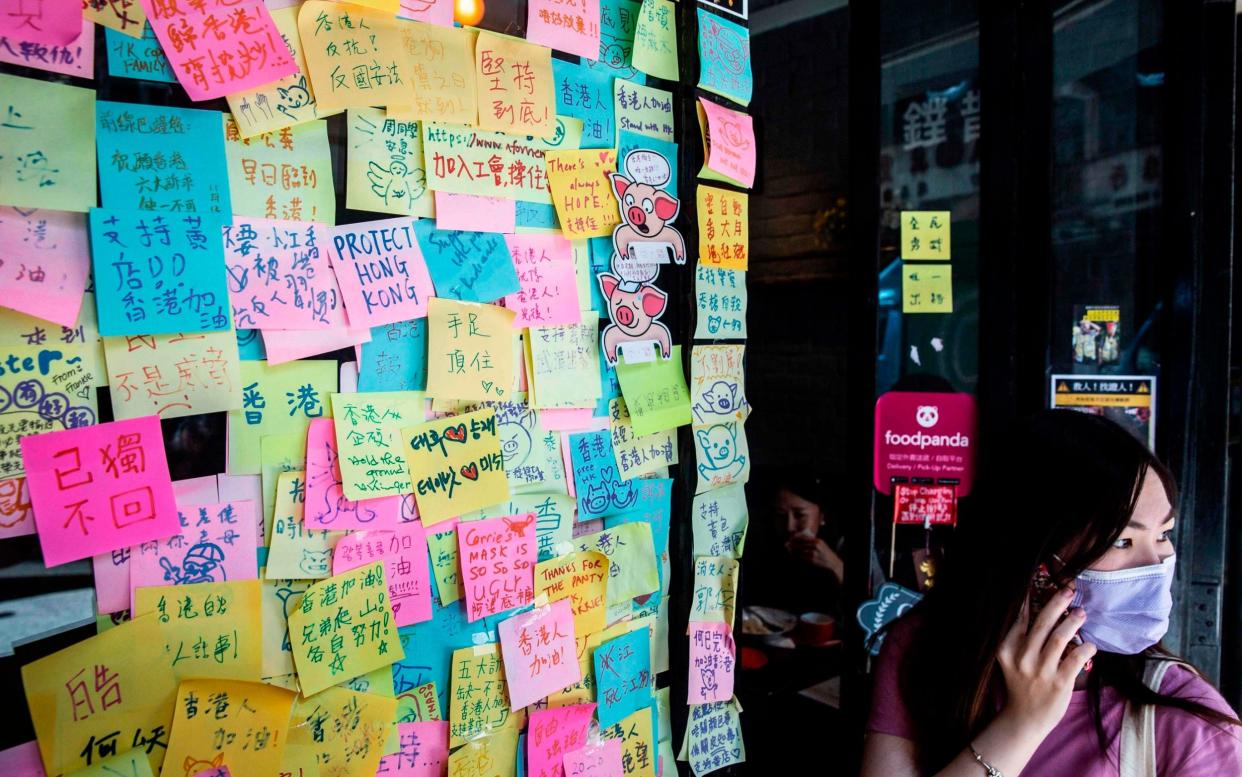 A woman (R) stands next to layers of notes on a Lennon Wall with messages of support for the pro-democracy protests outside a restaurant in Hong Kong - AFP