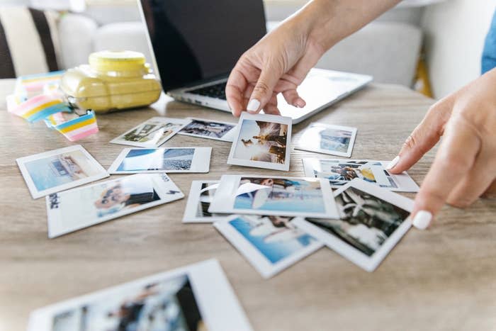 Person arranging a selection of printed photos on a table, with a laptop in the background