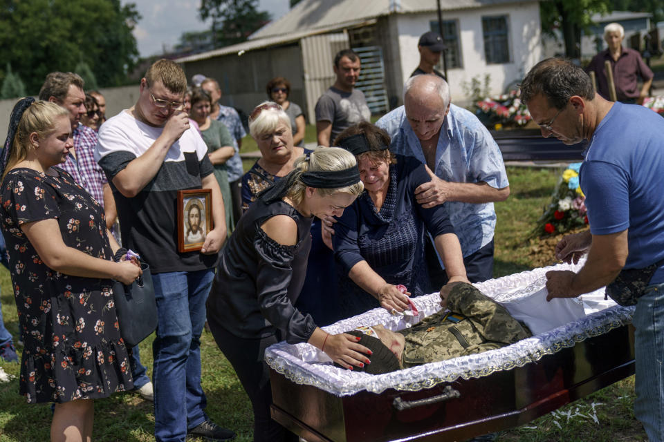 Lilia Panchenko is pulled away by her husband, Anatolii, right, as she says her final goodbye to their son, Oleh, along with his daughter, Ruslana, left, before his casket is covered during his burial service in Pokrovsk, Donetsk region, eastern Ukraine, Thursday, Aug. 4, 2022. Ukrainian soldier Oleh Panchenko, 48, was killed July 27 by Russian forces fighting in the Donetsk region. (AP Photo/David Goldman)