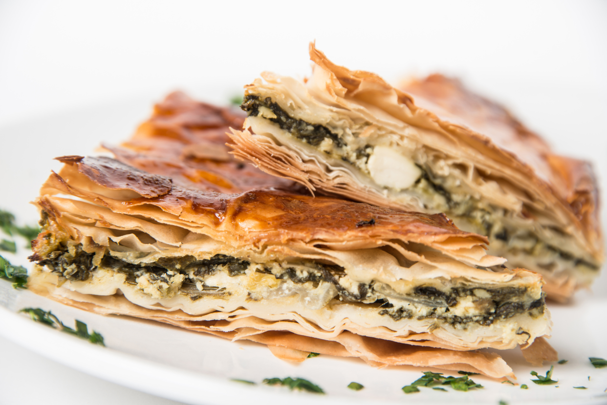 Closeup of two slices of easy Greek spinach pie for beginners, Spanakopita, on a white porcelain plate, selective focus, with a white background