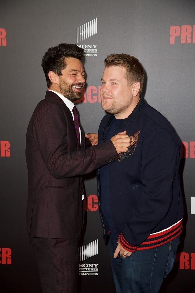 Two men smiling at each other at an event, one in a suit and the other in a casual jacket with embroidery