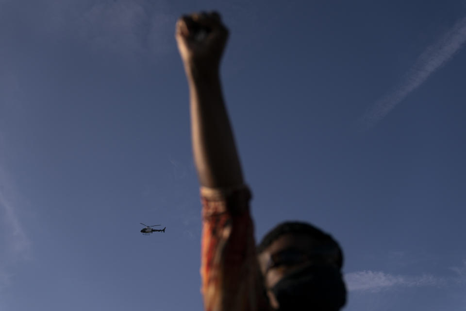 A Los Angeles Police helicopter hovers as Joyce Robertson, foreground, clenches her fist at the intersection of Florence and Normandie Avenues, Tuesday, April 20, 2021, in Los Angeles, after a guilty verdict was announced at the trial of former Minneapolis police Officer Derek Chauvin for the 2020 death of George Floyd. (AP Photo/Jae C. Hong)