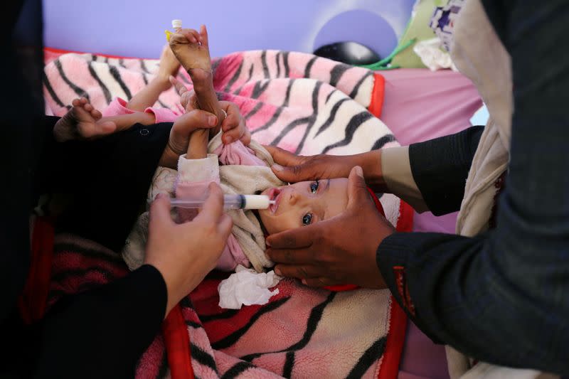 Man holds a malnourished girl as a woman feeds her at the malnutrition department of the al-Sabeen Maternity and Child Hospital in Sanaa