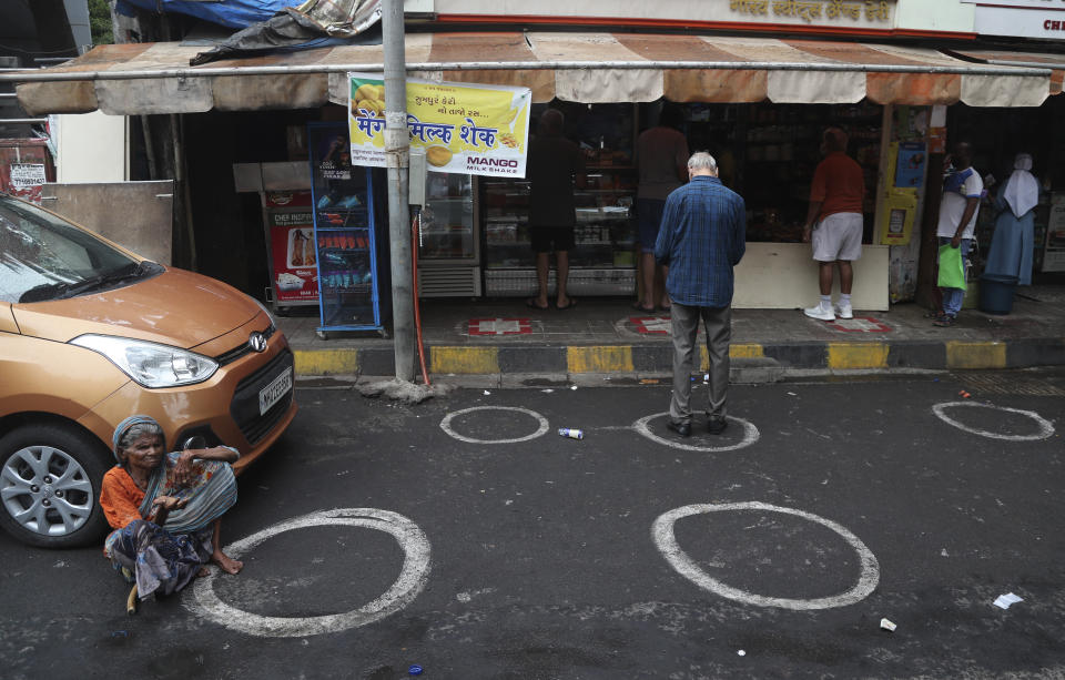 A woman sits asking for alms as people wait in a queue outside a grocery store in Mumbai, India, Monday, June 1, 2020. More states opened up and crowds of commuters trickled onto the roads in many of India's cities on Monday as a three-phase plan to lift the nationwide coronavirus lockdown started despite an upward trend in new infections. (AP Photo/Rafiq Maqbool)