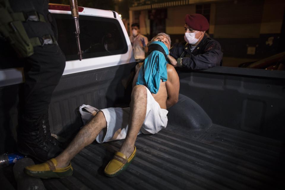 A police officer adjusts a t-shirt as a protective mask for a man they detained for violating the curfew amid coronavirus concerns in El Callao, on the outskirts of Lima, Peru, Wednesday, April 8, 2020. (AP Photo/Rodrigo Abd).