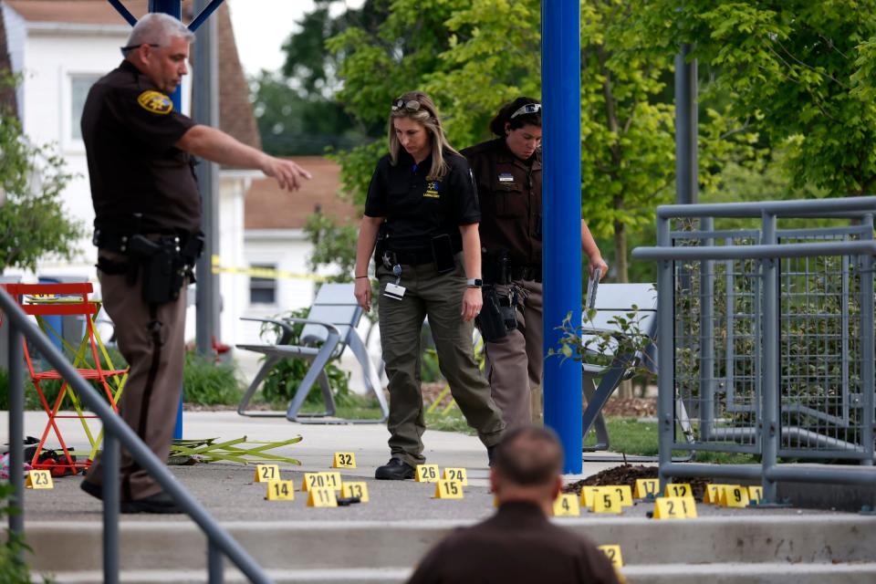 Police officers stand among yellow evidence markers mapping spent shell casings after a gunman opened fire at families at the Brooklands Plaza Splash Pad in Rochester Hills on Saturday. Nine people, including two children, were wounded.