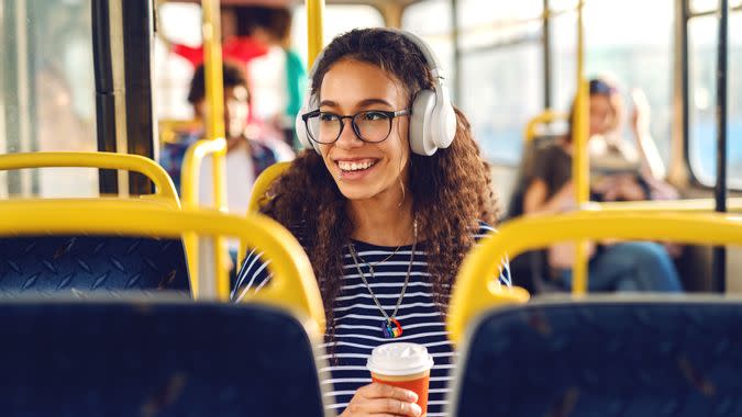 Girl sitting ina a bus drinking coffee, listening to music and looking trough window.