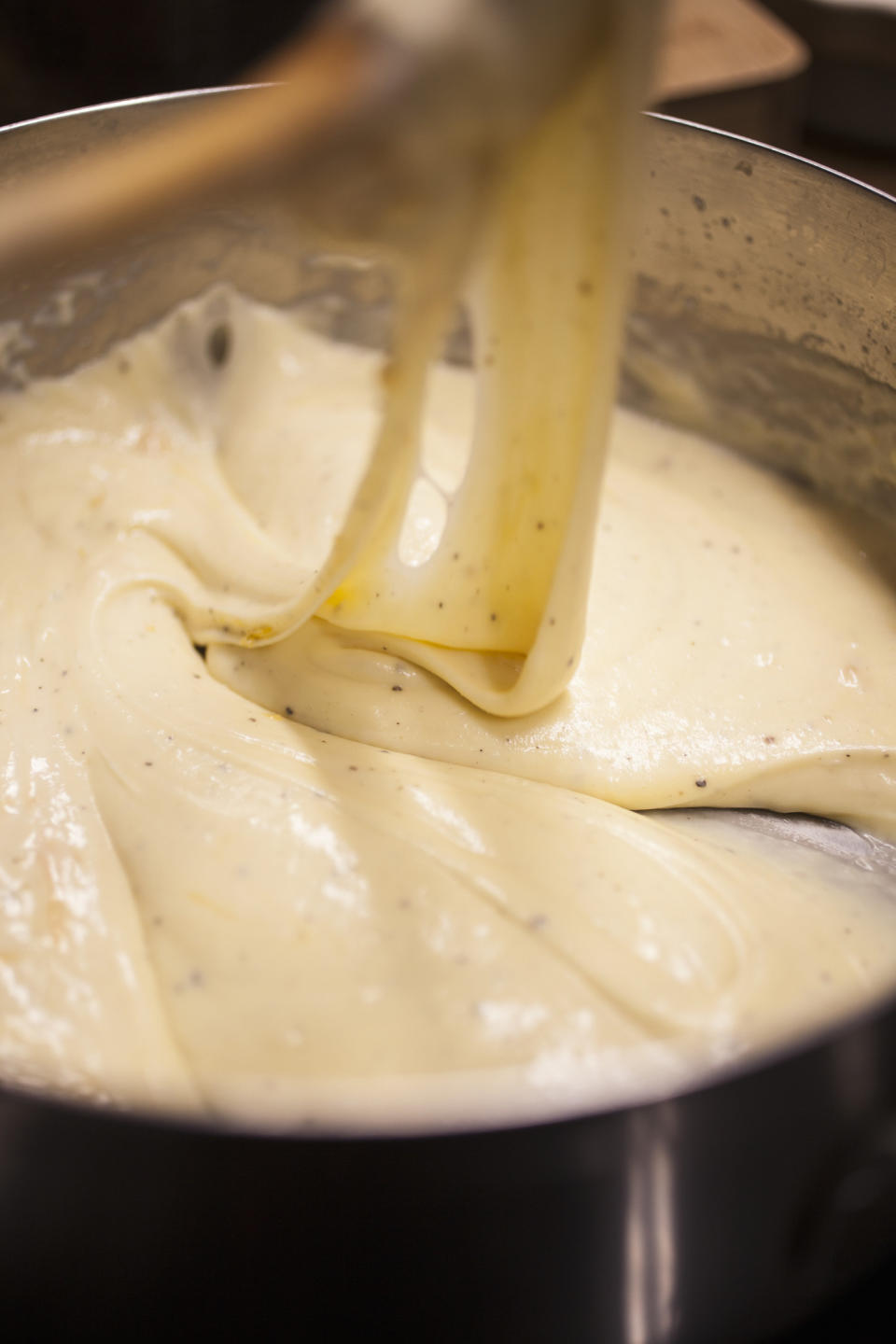 A cook preparing cheese sauce in a pot