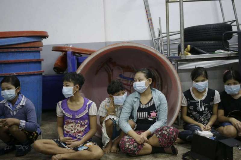 泰國中部龍仔厝府一家蝦子工廠，在工廠工作的兒童與青少年坐在地上，等待臨檢的警方登記（美聯社）
