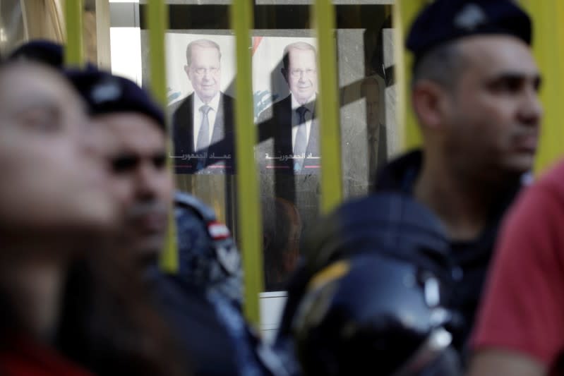 Pictures of Lebanese President Michel Aoun are seen at the state owned electricity company as police officers stand guard during ongoing anti-government protests in Beirut