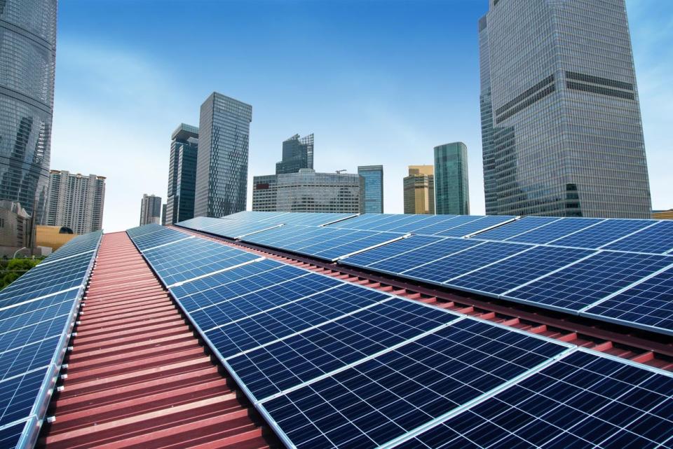 Solar panels are on a red roof against a city backdrop.