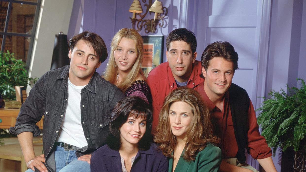 friends cast photo from season 1, including matt leblanc, lisa kudrow, david schwimmer, matthew perry, jennifer aniston, and courteney cox sitting on an armchair