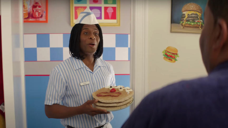 Kel Mitchell stands in a doorway holding a stack of smiling pancakes in Good Burger 2. 