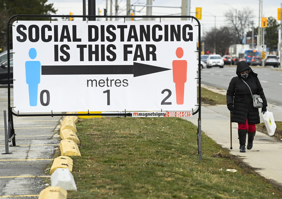 A person walks past a COVID-19 restrictions sign during the COVID-19 pandemic in Mississauga, Ontario, on Tuesday, Dec. 22, 2020. (Nathan Denette/The Canadian Press via AP)