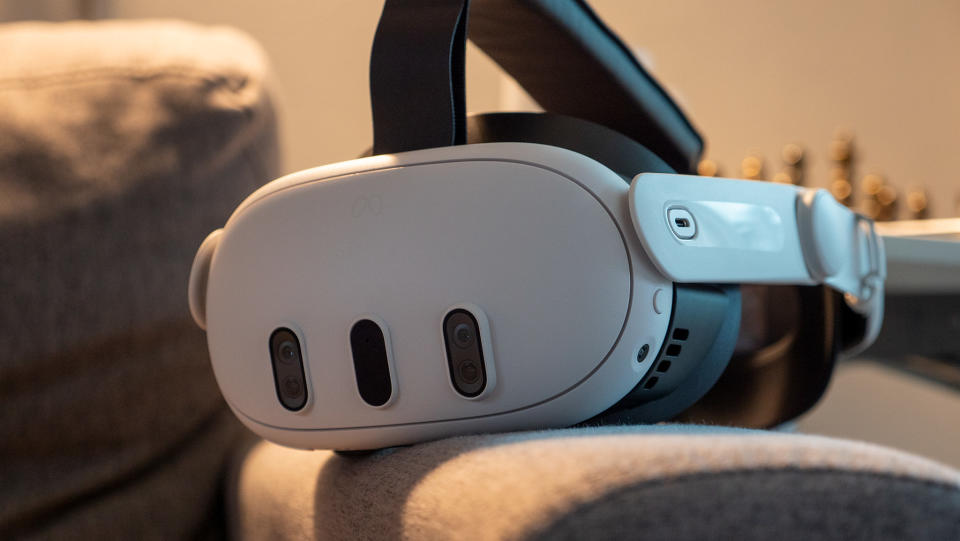 A Meta Quest 3 headset on the arm of a grey couch