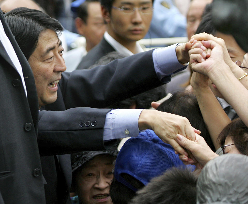 FILE - Japan's Chief Cabinet Secretary Shinzo Abe, left, reaches out for his supporters during his public speeches at Shibuya railway station in Tokyo Saturday, Sept. 16, 2006. Former Japanese Prime Minister Abe, a divisive arch-conservative and one of his nation's most powerful and influential figures, has died after being shot during a campaign speech Friday, July 8, 2022, in western Japan, hospital officials said.(AP Photo/Shuji Kajiyama, File)