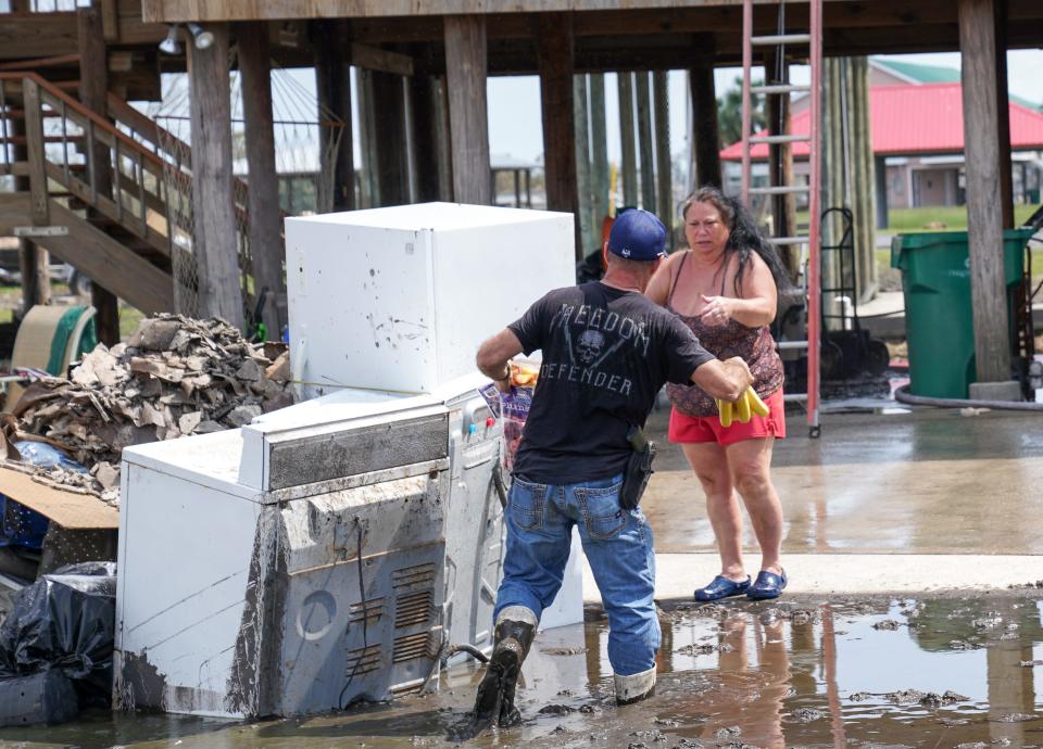 Wading through deep mud, Romeo Mamolo III hands fresh fruit to a woman stuck at her home on the island of Barataria, La. Barataria was cut off from the mainland after the passage of Hurricane Ida, and volunteers deliver food and other supplies to stranded residents.