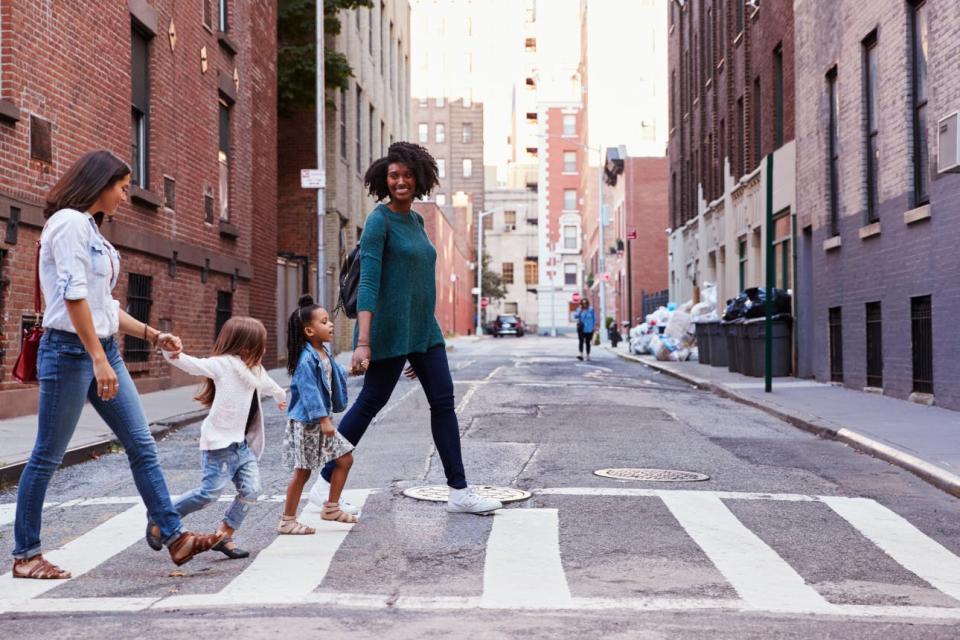 Two women cross a city street with their daughters