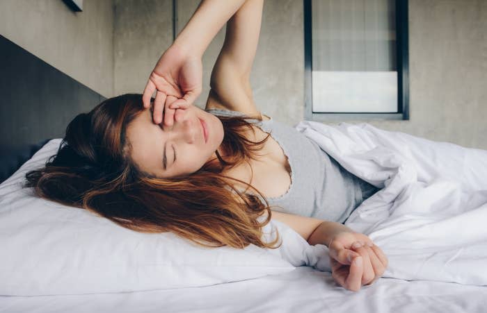 A person waking up in bed, rubbing their eyes. The scene suggests a morning routine