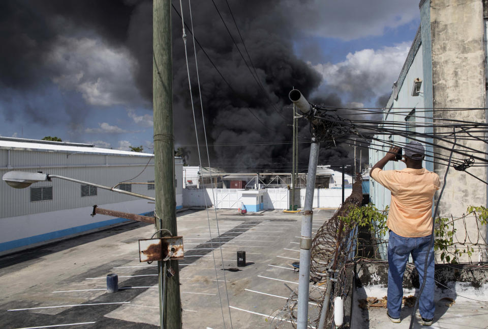 A resident makes a photo from a rooftop, of a black plume of smoke caused by a nearby explosion at the Polyplas plant in the Villas Agricolas neighborhood in Santo Domingo, Dominican Republic, Wednesday, Dec. 5, 2018. The mayor told reporters the fire began when a boiler exploded early Wednesday afternoon at the plastics company. Authorities say at least two people have died. (AP Photo/Tatiana Fernandez)