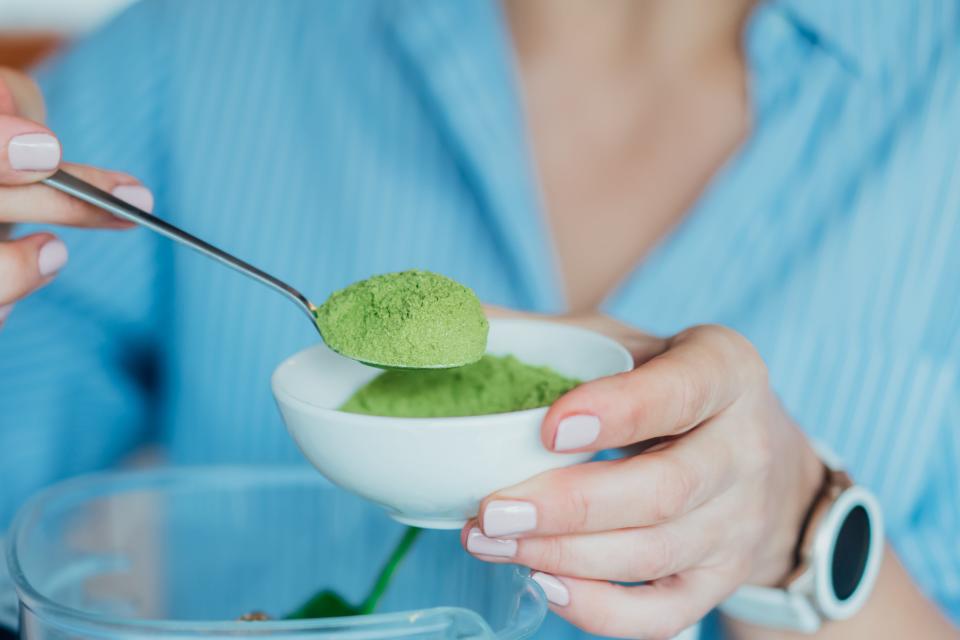 A person putting green powder in a smoothie.