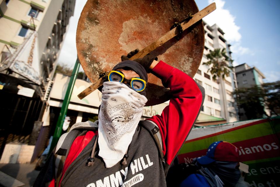 A demonstrator covers himself with a home made shield after policemen fired teargas during clashes in an anti-government protest in Caracas, Venezuela, Monday, March 10, 2014. The Venezuelan government and opposition appear to have reached a stalemate, in which street protests continue almost daily while the opposition sits out a peace process it calls farcical. (AP Photo/Alejandro Cegarra)