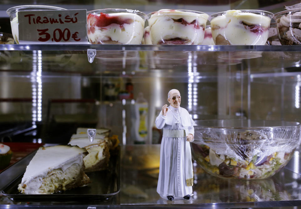 A statuette of Pope Francis is placed among desserts on sale at a cafe, in St. Peter's Square at the Vatican, Sunday, April 27, 2014. Tens of thousands of people have filled St. Peter's Square for a historic day of four popes, with Popes Francis and Benedict XVI honoring John XXIII and John Paul II by declaring them saints in the first ever canonization of two pontiffs. (AP Photo/Alessandra Tarantino)