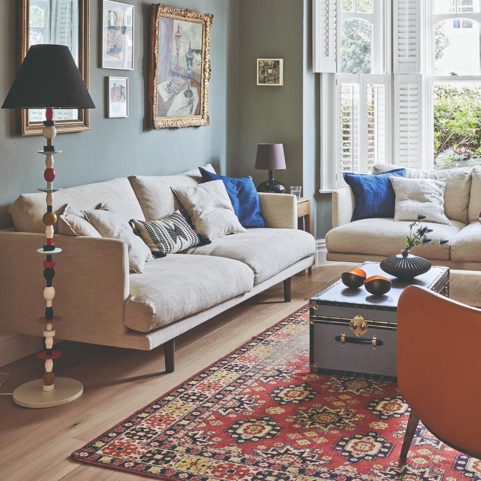 A green-painted living room with two cream sofas and a traditional trunk used as a coffee table