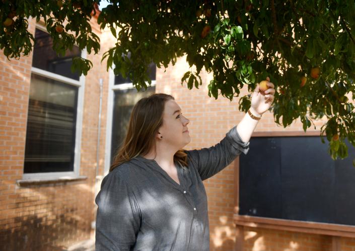 Alisa Palmer picks a peach off the tree in the Roscoe Wilson Magic Gardens, Friday, June 17, 2022. Palmer has two children who attend the elementary school.