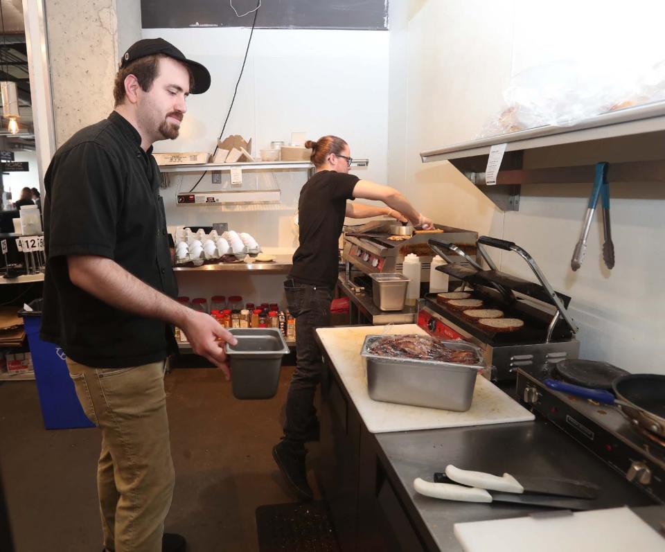 Former owner Sam LaVictoire, left, assists new co-owner Bill Simoes in preparing NOMZ signature sandwiches and other dishes March 23 at the Northside Marketplace restaurant in Akron.