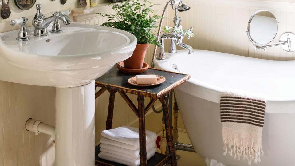 pedestal sink, clawfoot tub and gallery wall of antique bottle openers and art, walls painted gilded endive by valspar, small bathroom of 1940 craftsman cottage owned by landscape gardener anthony brewington in leighton, alabama