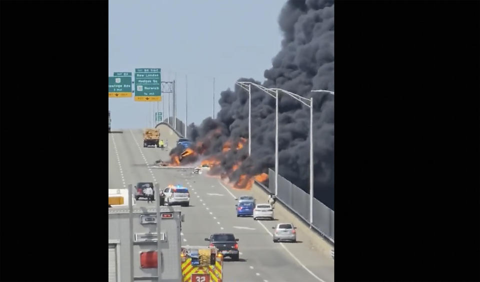 In this photo taken from video, smoke billows from the southbound edge of the Gold Star Bridge, Friday, April 21, 2023, in Groton, Conn. A crash involving a fuel truck and a car sparked a fire on the bridge, with flames spreading to buildings below and officials closing Interstate 95 in both directions during the blaze. Two people were taken to a hospital; the severity of their injuries wasn't immediately clear.(@sbottone/LOCAL NEWS X /TMX via AP)